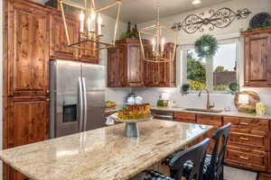 Kitchen with appliances with stainless steel finishes, tasteful backsplash, sink, light stone counters, and a notable chandelier