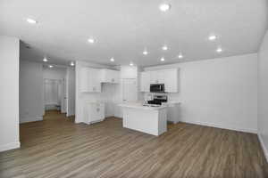 Kitchen with appliances with stainless steel finishes, white cabinets, sink, light hardwood / wood-style floors, and a kitchen island with sink