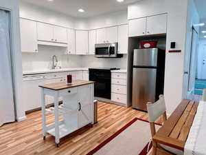 Kitchen with white cabinetry, light hardwood / wood-style flooring, and appliances with stainless steel finishes