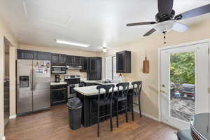 Kitchen featuring ceiling fan, appliances with stainless steel finishes, kitchen peninsula, a kitchen breakfast bar, and dark wood-type flooring