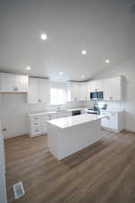 Kitchen featuring a kitchen island, white cabinetry, sink, dark hardwood / wood-style flooring, and stainless steel appliances