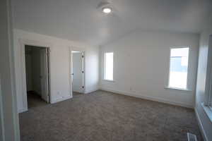 Unfurnished bedroom with dark colored carpet, lofted ceiling, and a spacious closet