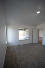 Carpeted empty room featuring lofted ceiling