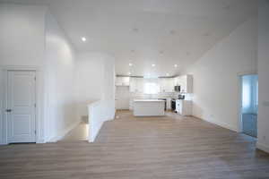 Unfurnished living room featuring sink, high vaulted ceiling, and light hardwood / wood-style flooring