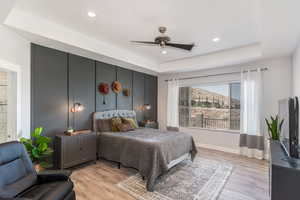 Bedroom with ceiling fan, light hardwood / wood-style flooring, and a raised ceiling