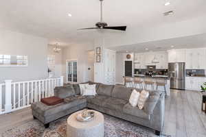 Living room with ceiling fan with notable chandelier and light hardwood / wood-style flooring