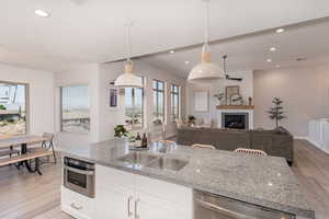 Kitchen with white cabinetry, light hardwood / wood-style flooring, light stone counters, stainless steel appliances, and sink