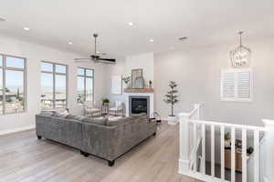 Living room featuring ceiling fan with notable chandelier and light wood-type flooring