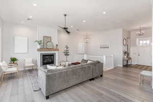 Living room with a fireplace, light hardwood / wood-style floors, and ceiling fan with notable chandelier