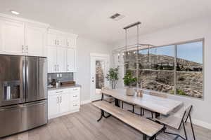 Kitchen with white cabinetry, hanging light fixtures, light hardwood / wood-style floors, and stainless steel refrigerator with ice dispenser