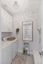 Laundry room featuring light tile patterned floors, independent washer and dryer, and cabinets