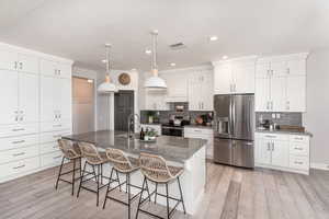 Kitchen featuring light wood-type flooring, white cabinets, backsplash, an island with sink, and stainless steel appliances