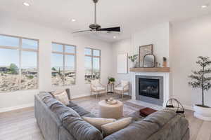 Living room with a large fireplace, ceiling fan, and light wood-type flooring