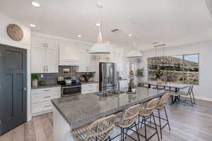 Kitchen featuring appliances with stainless steel finishes, light hardwood / wood-style flooring, backsplash, and white cabinetry