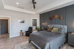 Bedroom featuring ensuite bath, ceiling fan, light wood-type flooring, and a tray ceiling