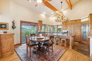 Dining space with high vaulted ceiling, ceiling fan with notable chandelier, light hardwood / wood-style floors, and beam ceiling