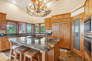 Kitchen featuring a notable chandelier, dark stone counters, a kitchen island, built in appliances, and decorative light fixtures