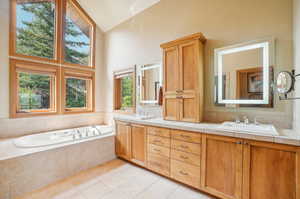 Bathroom with dual vanity, a wealth of natural light, tile patterned flooring, and high vaulted ceiling