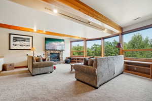 Living room featuring a stone fireplace, beamed ceiling, and carpet flooring