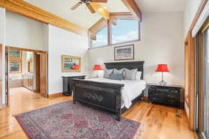 Bedroom with ceiling fan, ensuite bath, high vaulted ceiling, beam ceiling, and light hardwood / wood-style floors