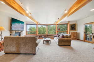 Living room with a stone fireplace, light colored carpet, and beam ceiling