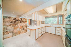 Kitchen with black oven, a textured ceiling, kitchen peninsula, light colored carpet, and sink