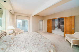 Bedroom with beamed ceiling, light colored carpet, and access to exterior