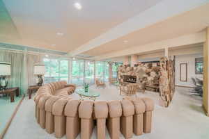 Living room with a stone fireplace, light carpet, a wall of windows, and a textured ceiling