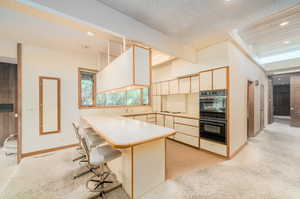 Kitchen featuring a breakfast bar, a textured ceiling, double oven, beamed ceiling, and light carpet