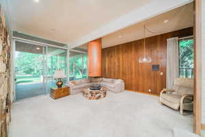 Carpeted living room featuring plenty of natural light, beamed ceiling, a textured ceiling, and wooden walls