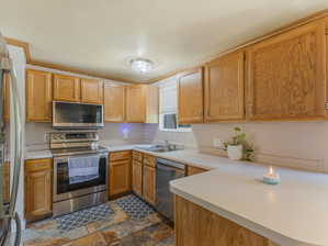 Kitchen with stainless steel appliances, sink, dark tile patterned flooring, and kitchen peninsula