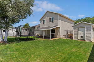 Rear view of property featuring a storage unit, a patio area, a trampoline, and a yard