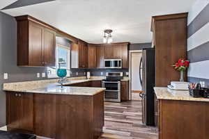 Kitchen with light hardwood / wood-style floors, kitchen peninsula, light stone counters, and stainless steel appliances