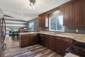 Kitchen with dishwashing machine, black refrigerator, dark hardwood / wood-style flooring, vaulted ceiling, and kitchen peninsula