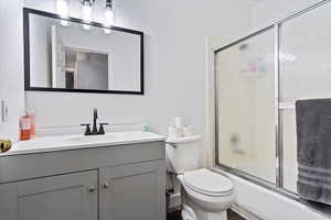 Full bathroom with bath / shower combo with glass door, toilet, and vanity