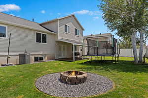 Rear view of house with a yard, central air condition unit, a trampoline, and a fire pit