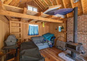 Living room featuring vaulted ceiling with beams, a wood stove, wood walls, brick wall, and wood-type flooring