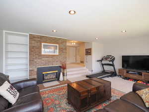 Living room featuring a fireplace, built in shelves, carpet, and brick wall