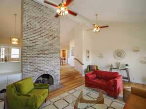 Living room with a fireplace, ceiling fan with notable chandelier, light wood-type flooring, and high vaulted ceiling