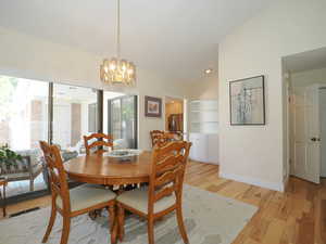 Dining room with a notable chandelier, light hardwood / wood-style flooring, lofted ceiling, and built in features