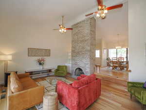 Living room with ceiling fan with notable chandelier, light hardwood / wood-style floors, brick wall, and a fireplace