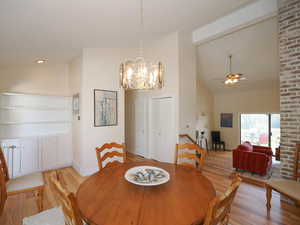 Dining room featuring high vaulted ceiling, brick wall, ceiling fan with notable chandelier, and light hardwood / wood-style floors