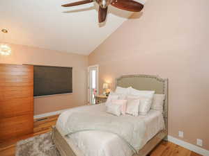 Bedroom featuring light hardwood / wood-style floors, ceiling fan with notable chandelier, and high vaulted ceiling