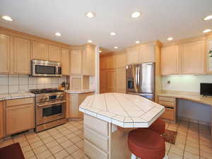 Kitchen with a center island, tile counters, tasteful backsplash, and appliances with stainless steel finishes