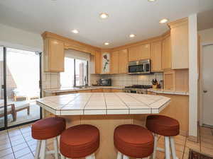 Kitchen featuring range, decorative backsplash, sink, tile counters, and light tile patterned floors