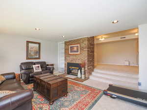 Living room featuring a brick fireplace, brick wall, and carpet floors