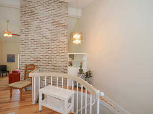 Stairway featuring an inviting chandelier, high vaulted ceiling, brick wall, and wood-type flooring