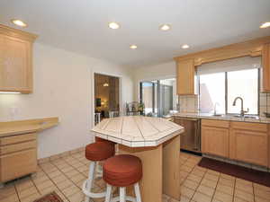 Kitchen featuring sink, dishwasher, a kitchen island, tile countertops, and light tile patterned floors