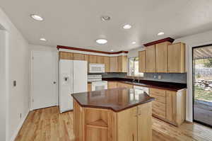 Kitchen with white appliances, sink, a kitchen island, light hardwood / wood-style floors, and backsplash