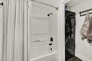 Bathroom with wood walls, tile patterned floors, shower / bath combo with shower curtain, and stacked washing maching and dryer